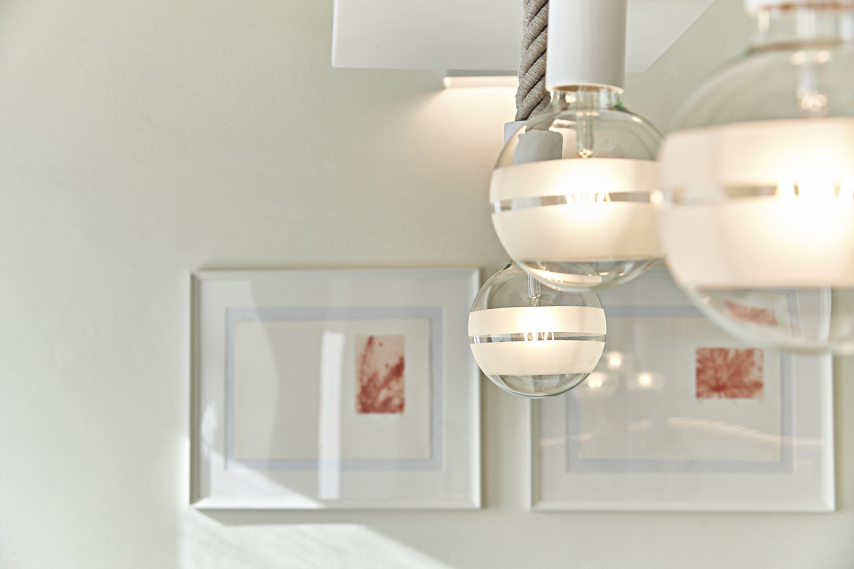 A modern chandelier with multiple spherical lights and a white wall with framed artwork.