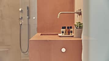Een badkamer met een houten wastafelmeubel, een douche en een kleine potplant.