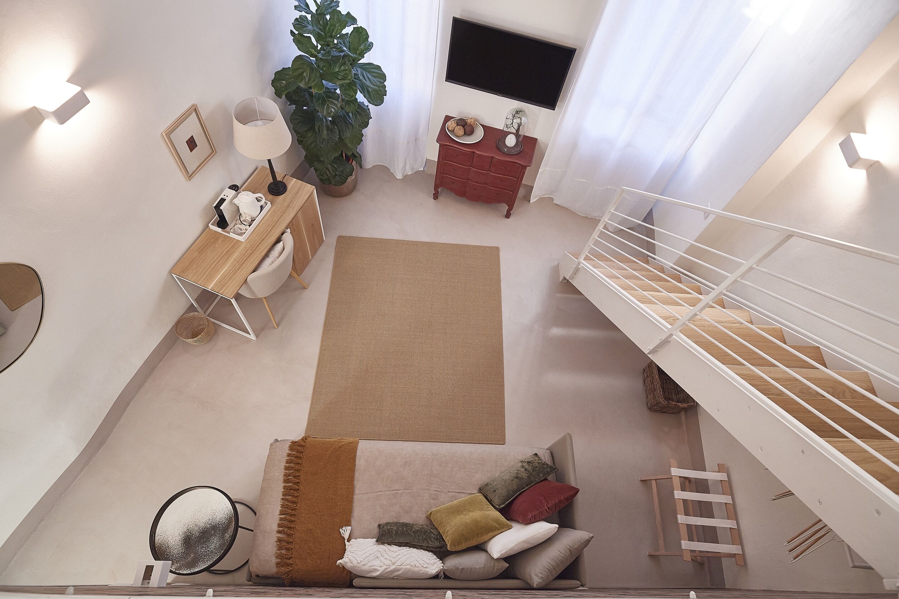 Una sala de estar moderna con un sofá, una mesa de centro, una planta grande, un televisor y una escalera.
