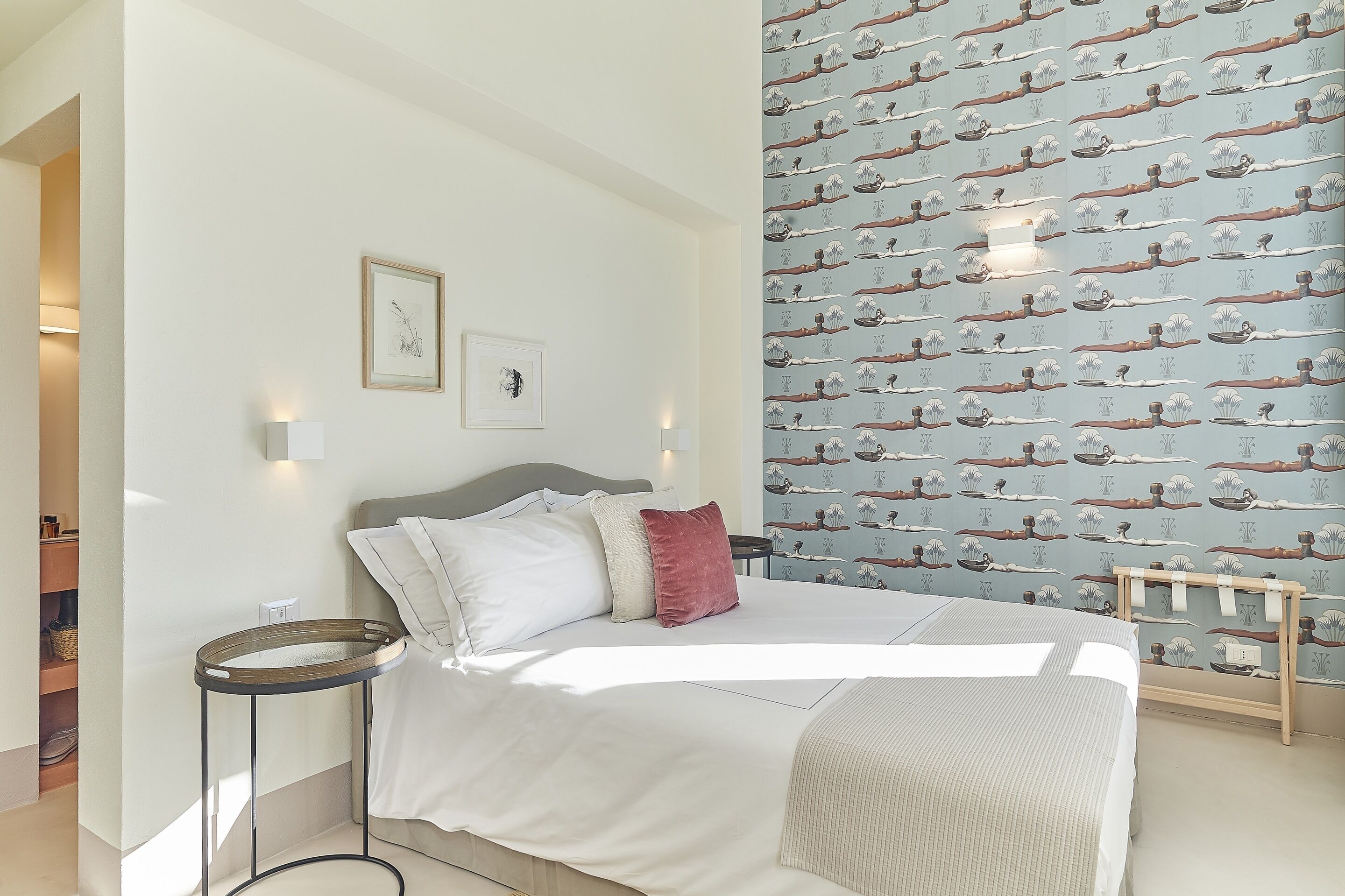 A neatly made bed with pillows, a bedside table, and a wall with a patterned wallpaper.