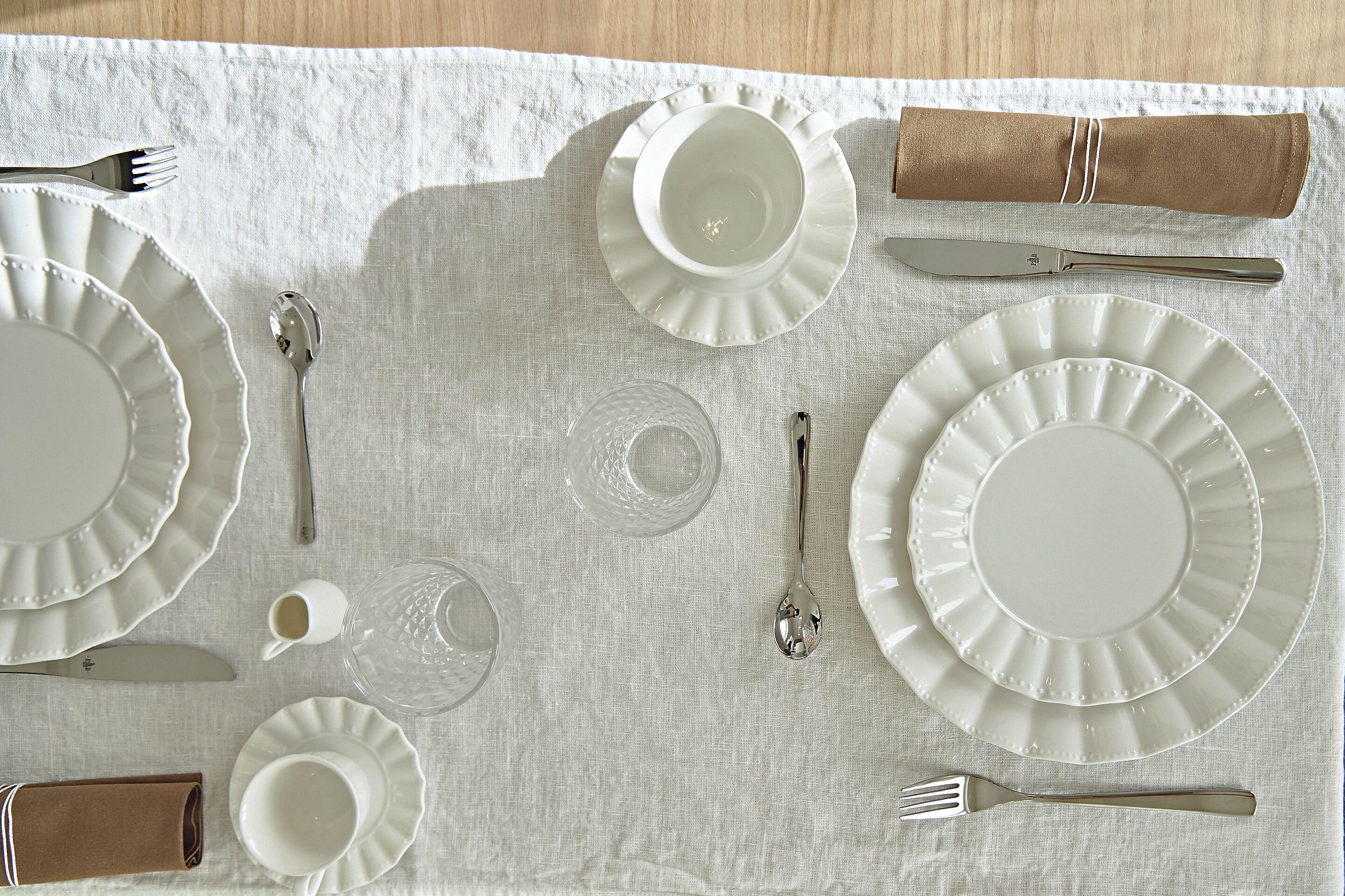 Une table mise avec soin, avec des assiettes, des couverts et une serviette sur une nappe blanche.