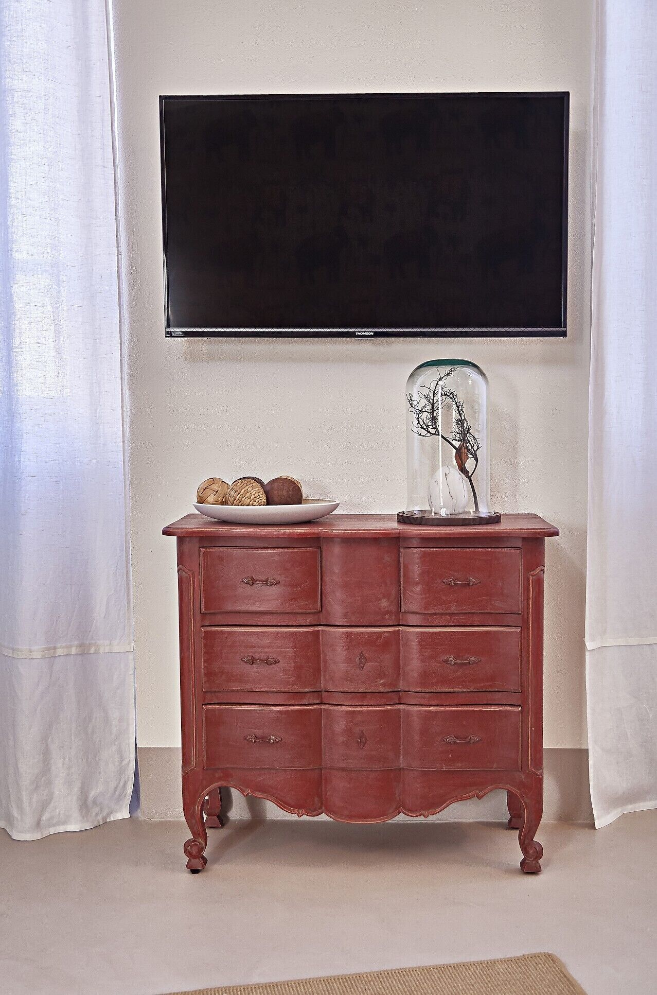 Une commode en bois avec des tiroirs, un vase en verre orné de branches et une assiette décorative.