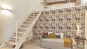 A bedroom with a bed, a sofa, a staircase, and a wall with elephant and palm tree wallpaper. - Dora maison de charme (Ivrea)