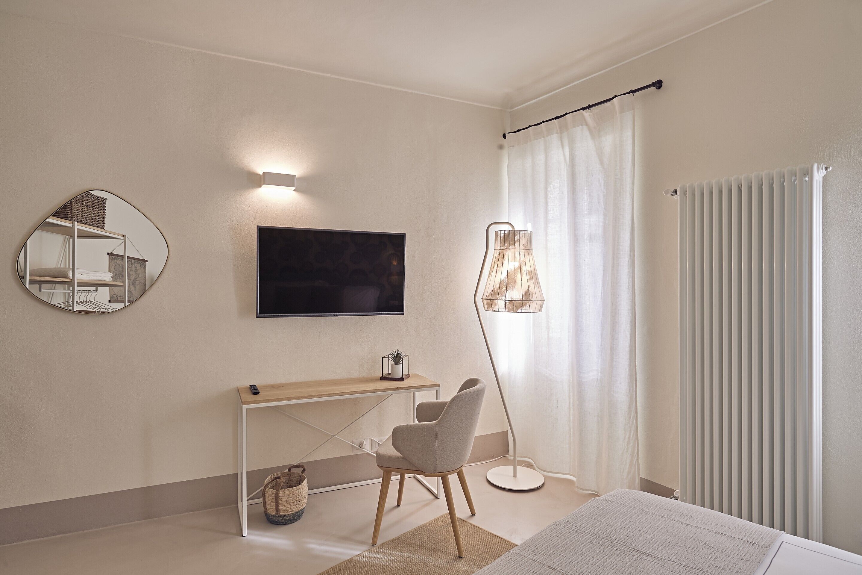 Un dormitorio moderno con una cama, un escritorio, una silla, un televisor, una lámpara de pie y un radiador.