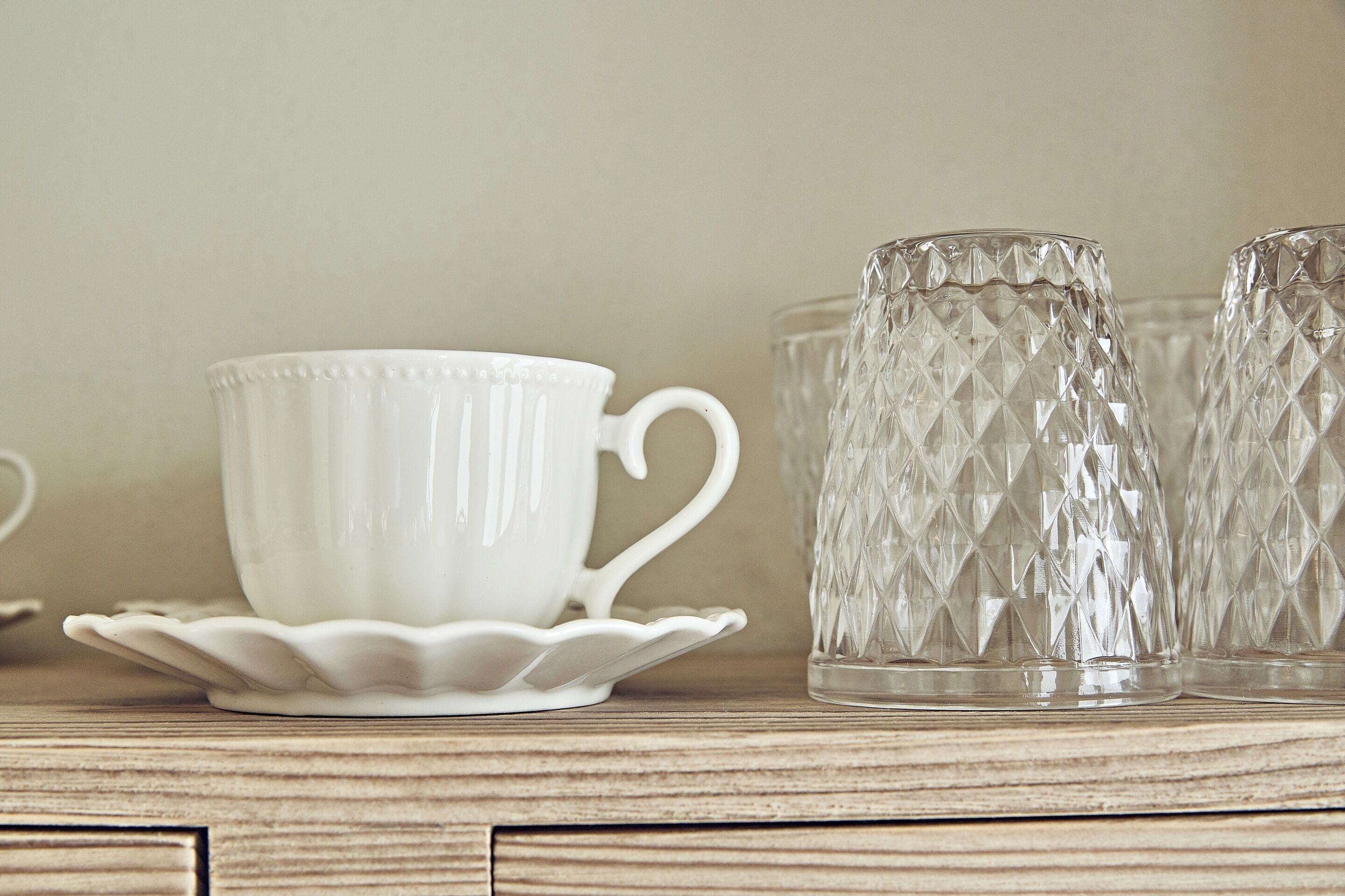 Una taza y platillo de cerámica blanca sobre una superficie de madera, acompañados por dos jarrones de vidrio transparente con diseño de diamantes.