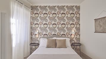 Una cama bien hecha con sábanas blancas y dos almohadas color beige, una pared con un estampado de globos aerostáticos, y dos mesitas de noche con lámparas.