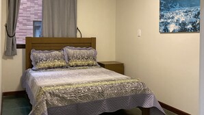 A bedroom with a bed, a ceiling fan, a window with curtains, and a painting on the wall. - Apartment in Praia Grande 100 m from the beach (Ubatuba)