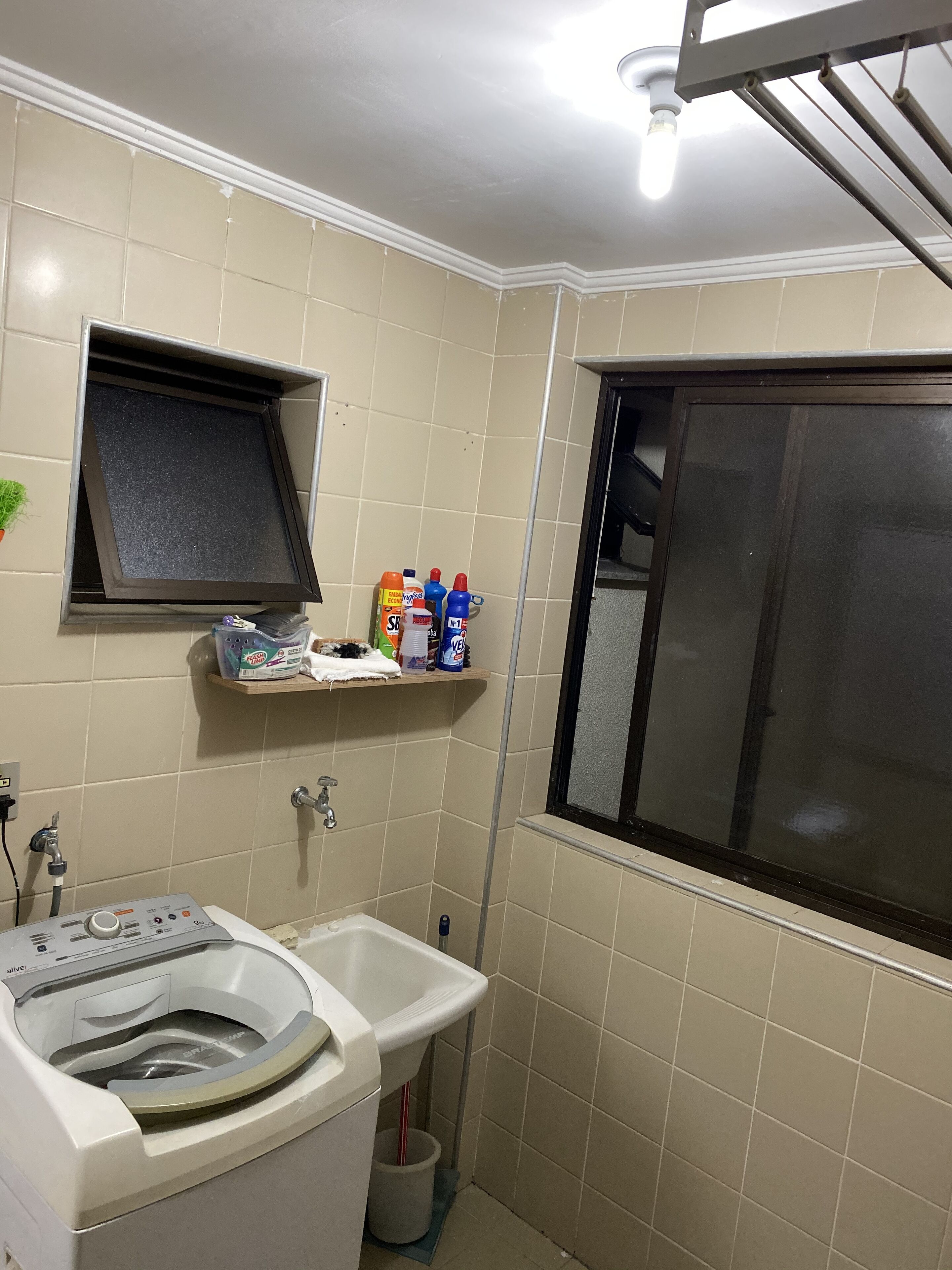 A compact bathroom with a washing machine, a sink, and a shelf with cleaning supplies.