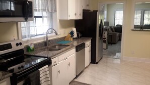 A kitchen with a stove, microwave, sink, and cabinets. There is a window with curtains, a countertop with a knife block, and a refrigerator. - COOL HAVEN- A Quiet, Elegant, Contemporary, Incognito Retreat near FAMU/FSU (Tallahassee)