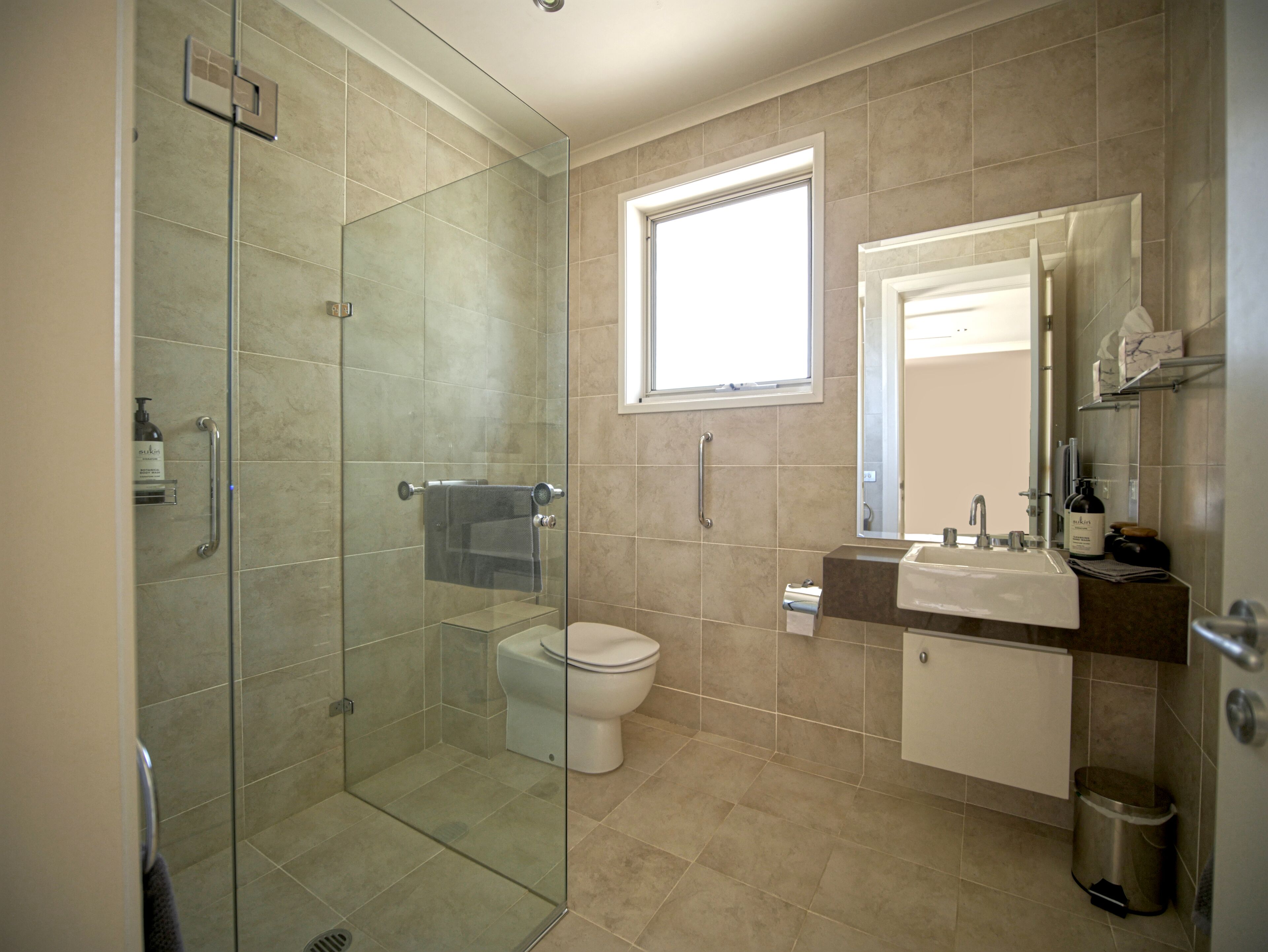 Een moderne badkamer met een douche met glazen wand, een toilet en een wastafel met spiegel erboven.