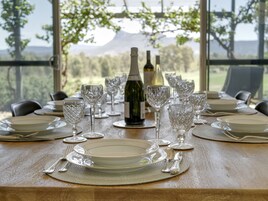 Uma mesa posta para refeição com garrafas de vinho e copos, com vista panorâmica.