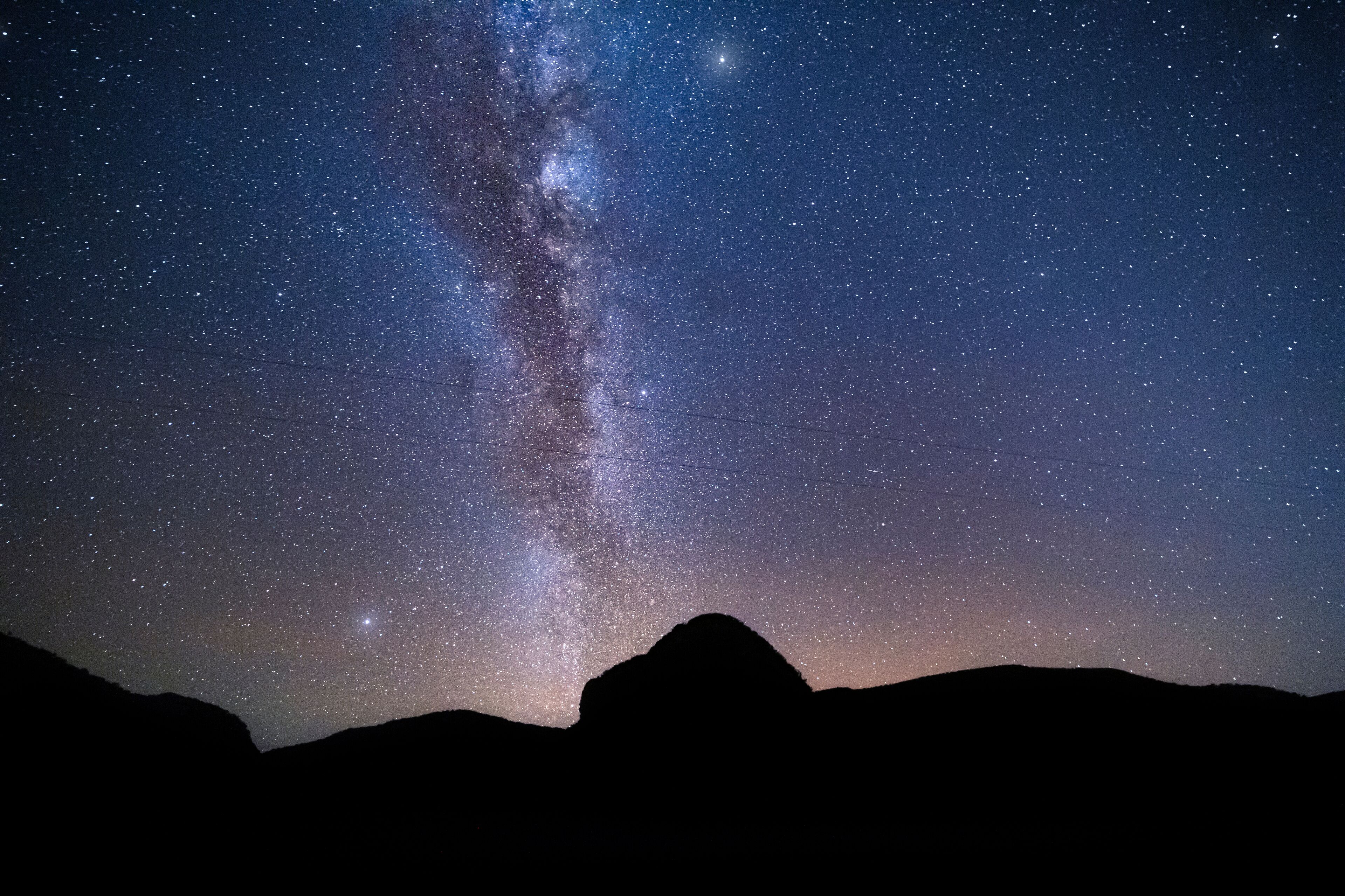 Cielo nocturno con estrellas y la Vía Láctea visible sobre el perfil de una montaña.