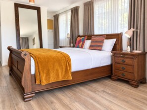 A bedroom with a wooden bed, a bedside table with drawers, a lamp, and a mirror. - George Bass Drive 569 On The Beach Living (Malua Bay)