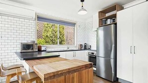 Eine moderne Küche mit einer Holzinsel, weißen Schränken, einem Edelstahlkühlschrank und einem Fenster mit Blick auf Grünflächen.