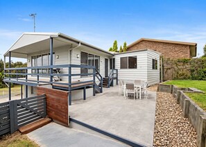 A modern two-story house with a covered patio, outdoor seating, and a fenced garden area.