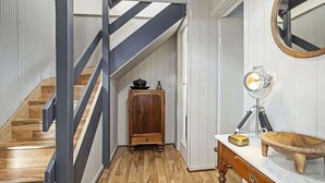 Ein Flur mit Holzboden, einer Treppe mit dunklen Geländern, einem Holzschrank, einem Tisch mit einer Schüssel und einem Spiegel.