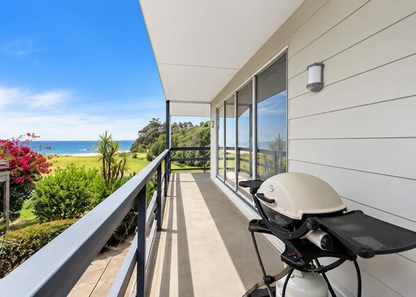 A balcony with a grill, overlooking a beach and greenery. - George Bass Drive 569 On The Beach Living (Malua Bay)