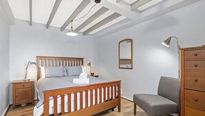 Ein Schlafzimmer mit einem hölzernen Bett, Nachttischen, einem Sessel, einem Schminktisch und einem Spiegel.