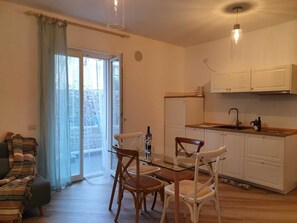 Un espace de vie compact comprenant un coin repas, une cuisine et des portes-fenêtres coulissantes donnant sur un balcon.