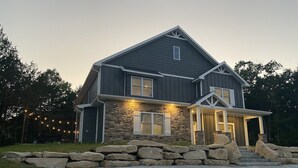 Une maison à deux étages, avec des fondations en pierre, un porche à l’avant et une allée.