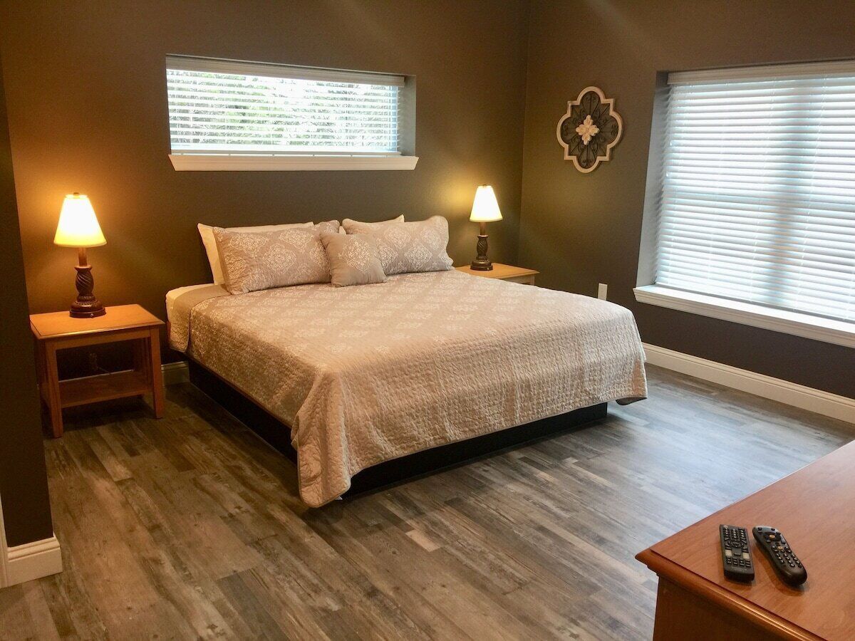 A bedroom with a bed, two bedside tables with lamps, a wooden nightstand, and a wooden dresser.