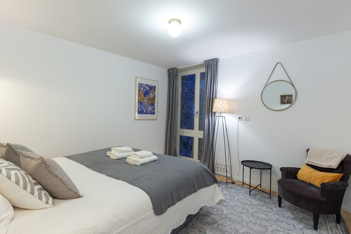 A neatly arranged hotel room with a bed, a chair, a small table, and a floor lamp.