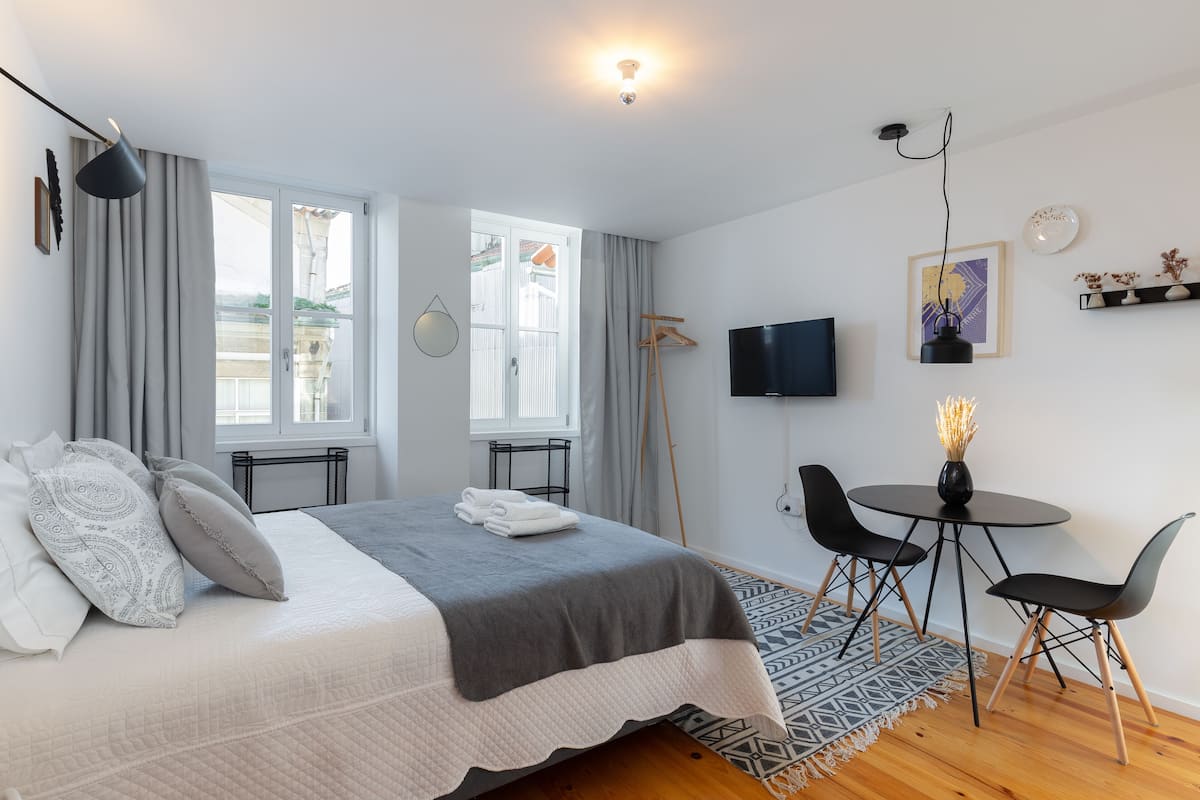 A modern bedroom with a large bed, a TV, a small dining table, and a view of the outside.