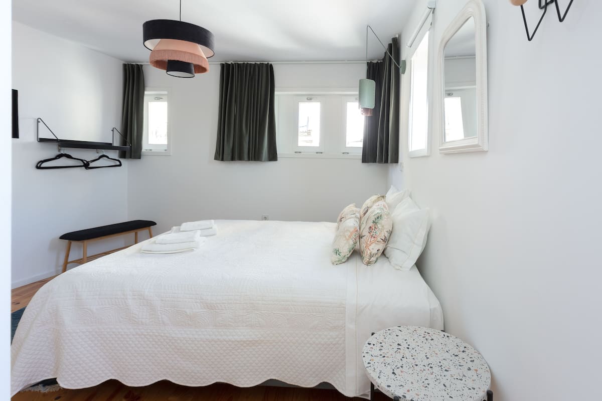 A bedroom with a bed, a bench, a round table, and a mirror.