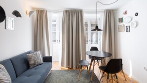 A modern living room with a blue sofa, a round table with chairs, and a large window with curtains. - Porto Belomonte Studios (Porto)