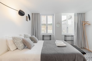 Quarto moderno com cama, mesas de cabeceira, luminária pendente e vista para o exterior.