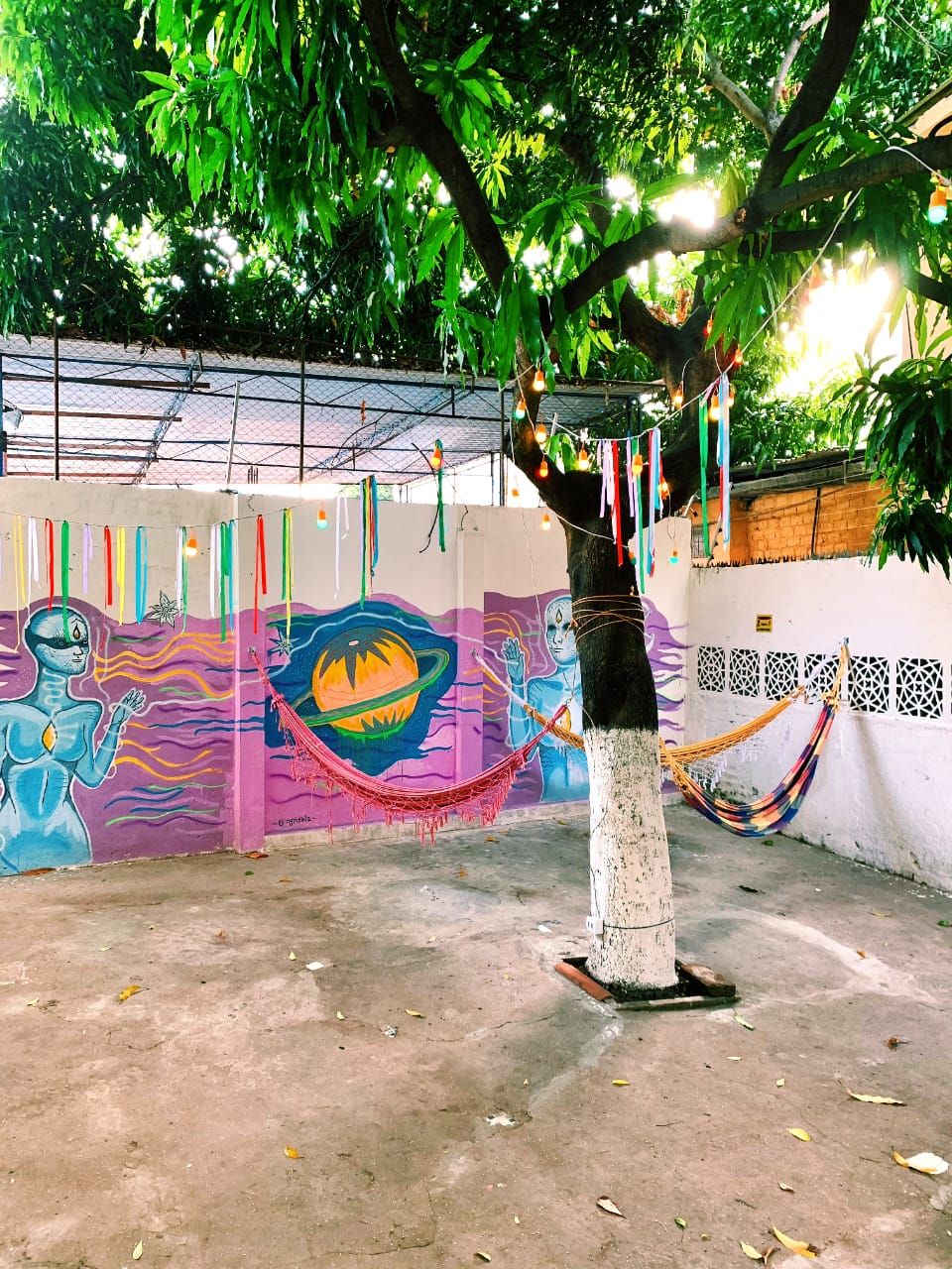 A hammock under a tree with a colorful mural in the background.