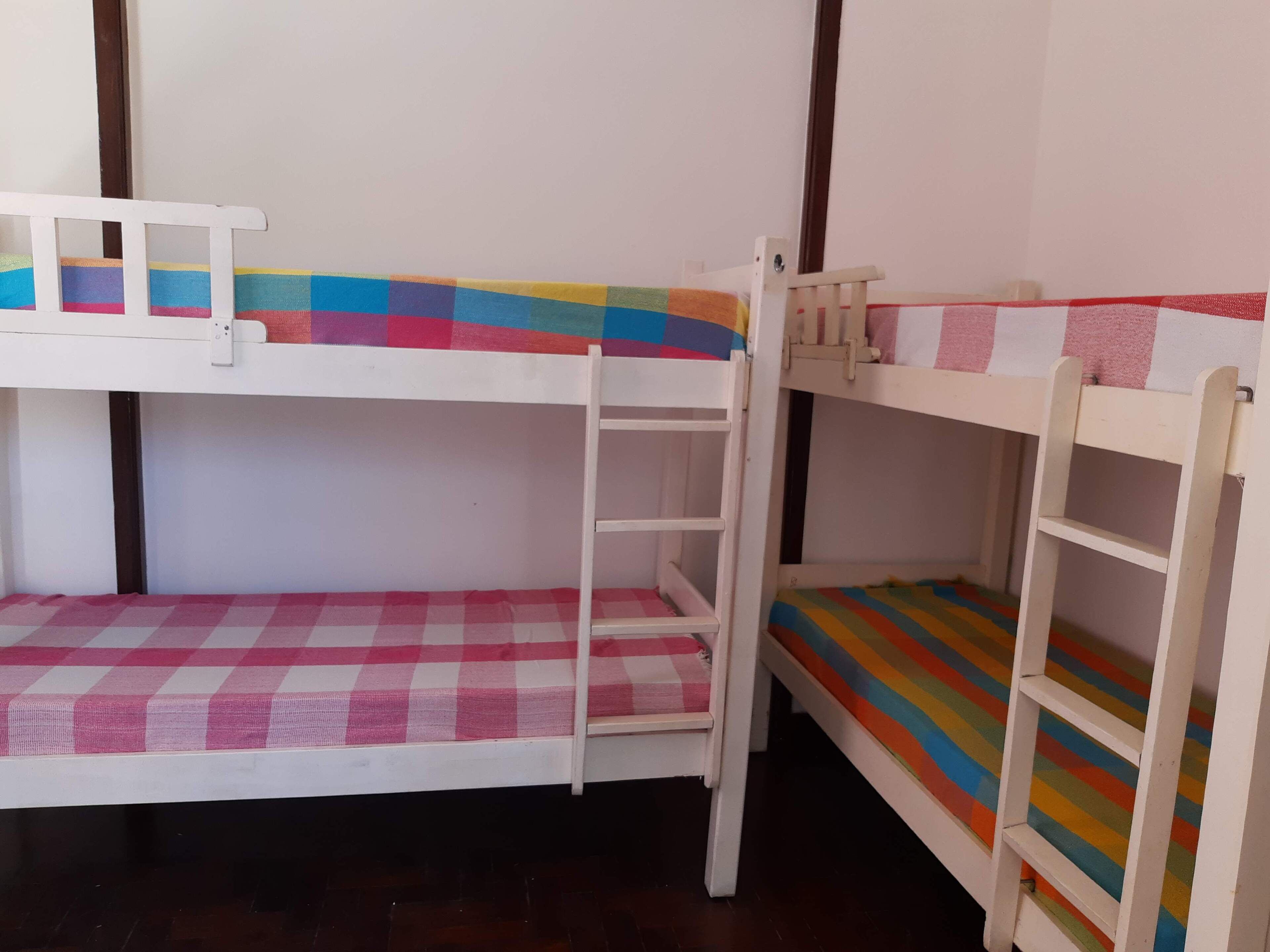 A bunk bed room with a checkered pink and white floor, a colorful striped bedspread, and a white ladder.