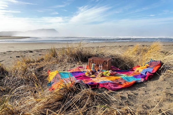 A beach picnic setup with a blanket, basket, and food items.