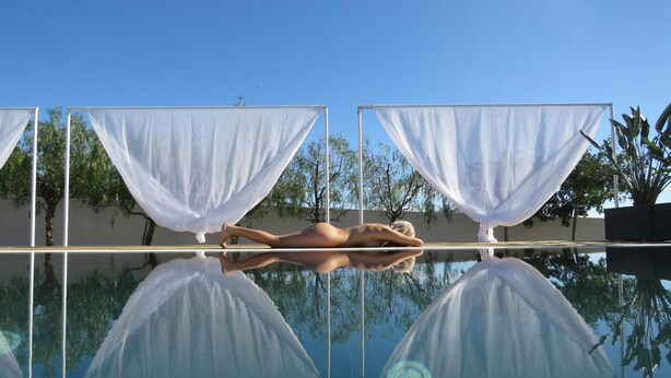 Ein Pool mit klaren Spiegelungen, umgeben von weißen Vorhängen und Bäumen.