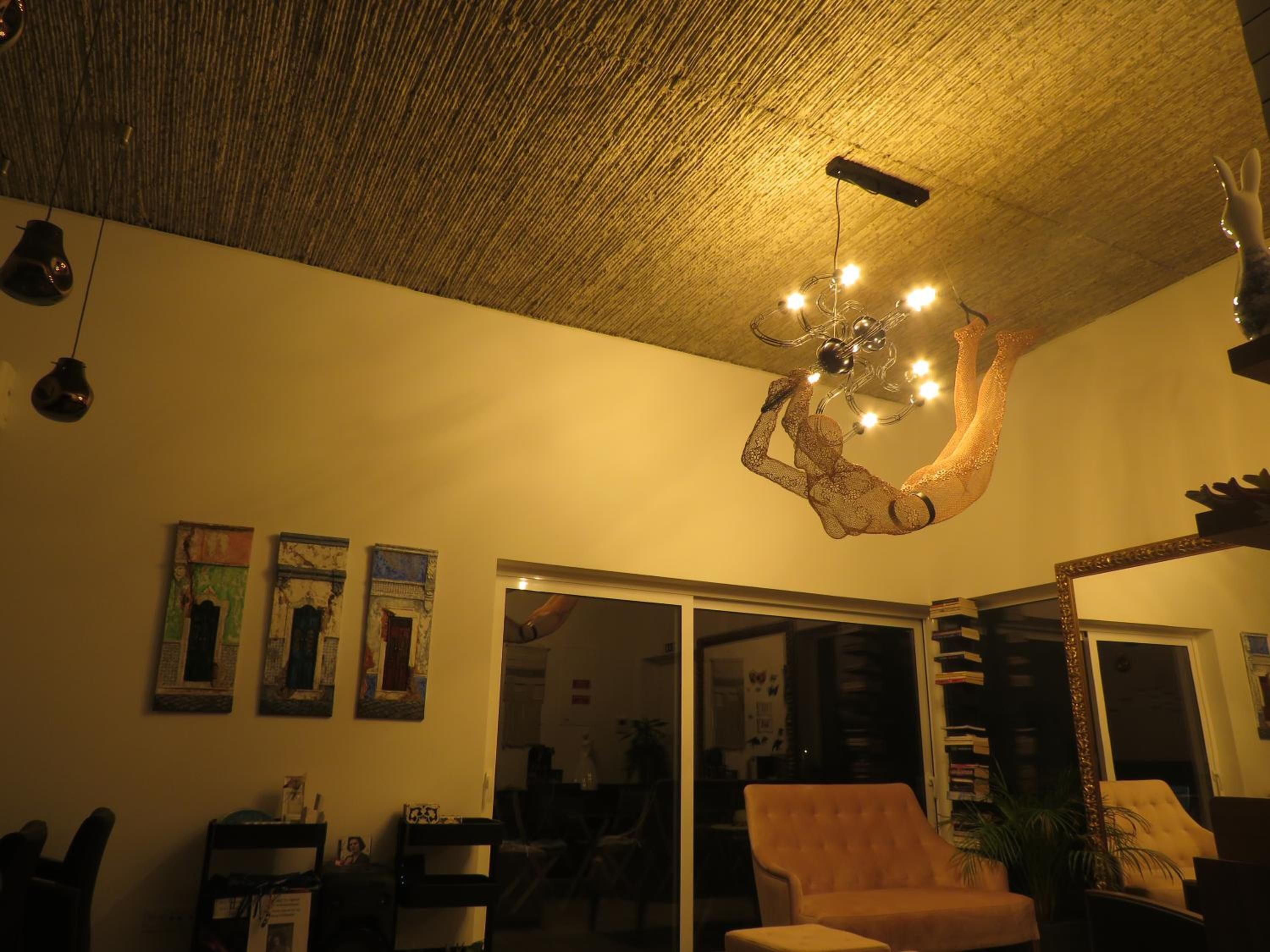 Una sala de estar con techo de madera, un candelabro, un ventanal corredero y una estantería.