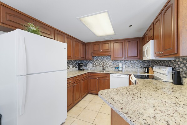 Una cocina con armarios de madera, un refrigerador blanco, un microondas, una estufa y salpicadero de azulejos.