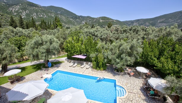 A pool area with stone flooring, lounge chairs, umbrellas, and a view of a mountainous landscape. - Calderimi - Lefkada Rooms (Lefkada)