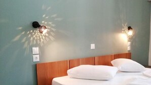 A neatly made bed with white linens, a wooden headboard, and two wall-mounted light fixtures casting shadows on the wall. - Calderimi - Lefkada Rooms (Lefkada)