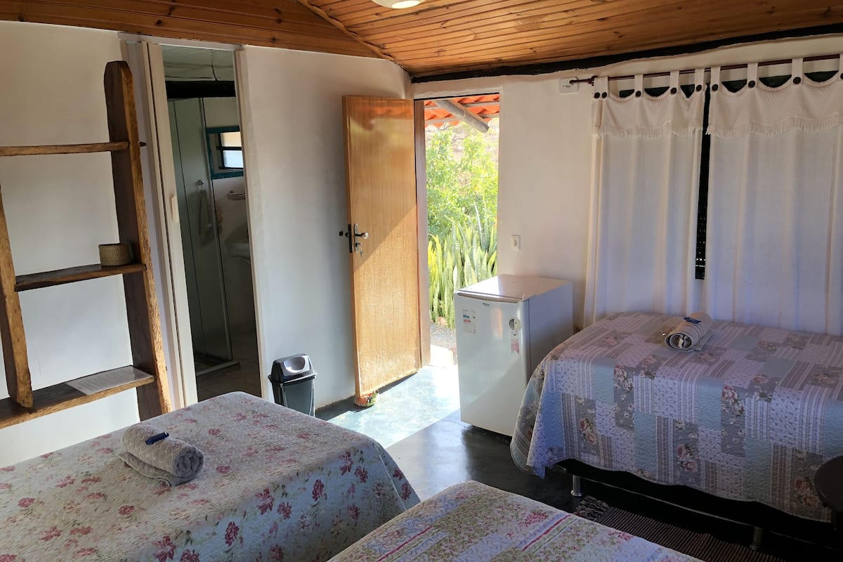 A room with two beds, a small refrigerator, a trash bin, and a door leading outside.