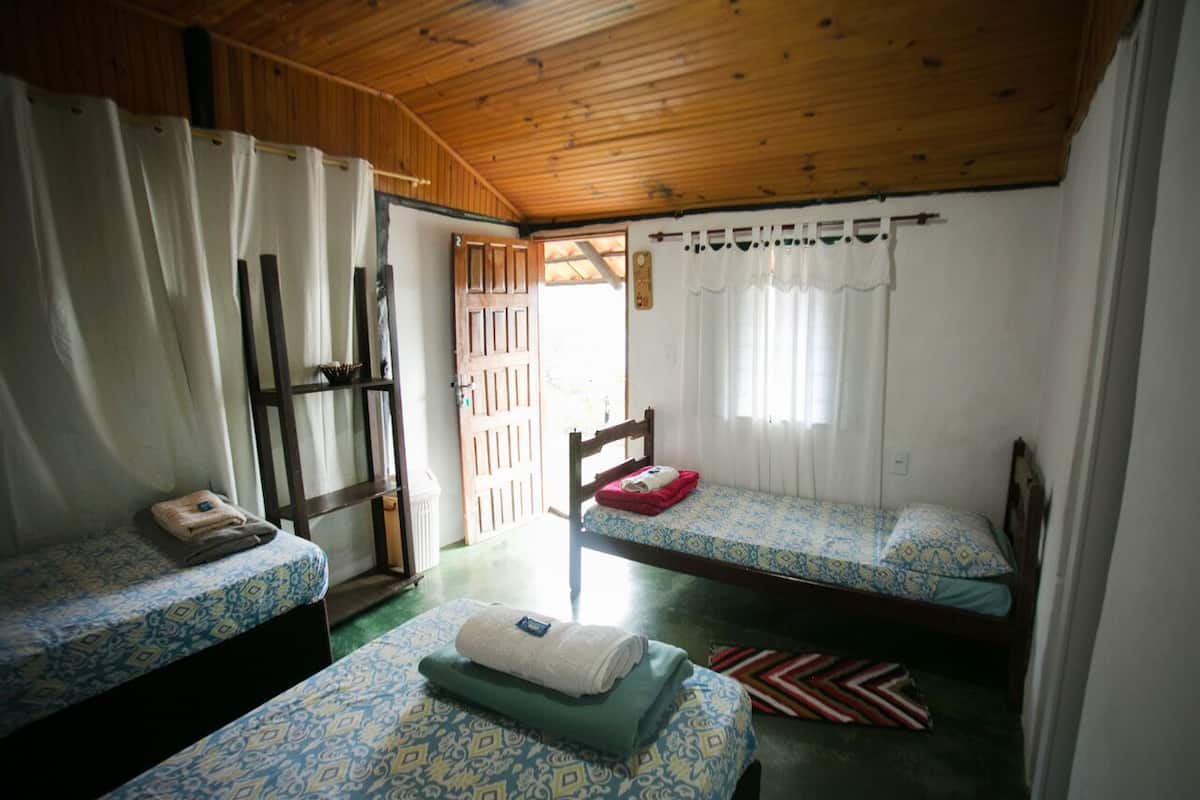 A small, cozy room with two single beds, a wooden ceiling, and a window with curtains.
