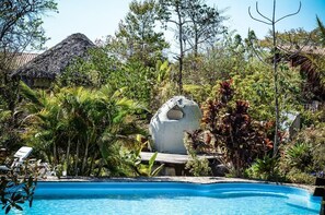 Una piscina rodeada de exuberante vegetación y una estructura esférica singular.