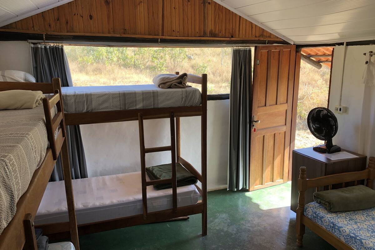 A bunk bed room with a wooden ceiling, a fan, and a view of the outdoors.