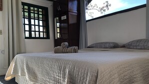 Un dormitorio con cama, almohadas, una ventana con cortinas y un armario.