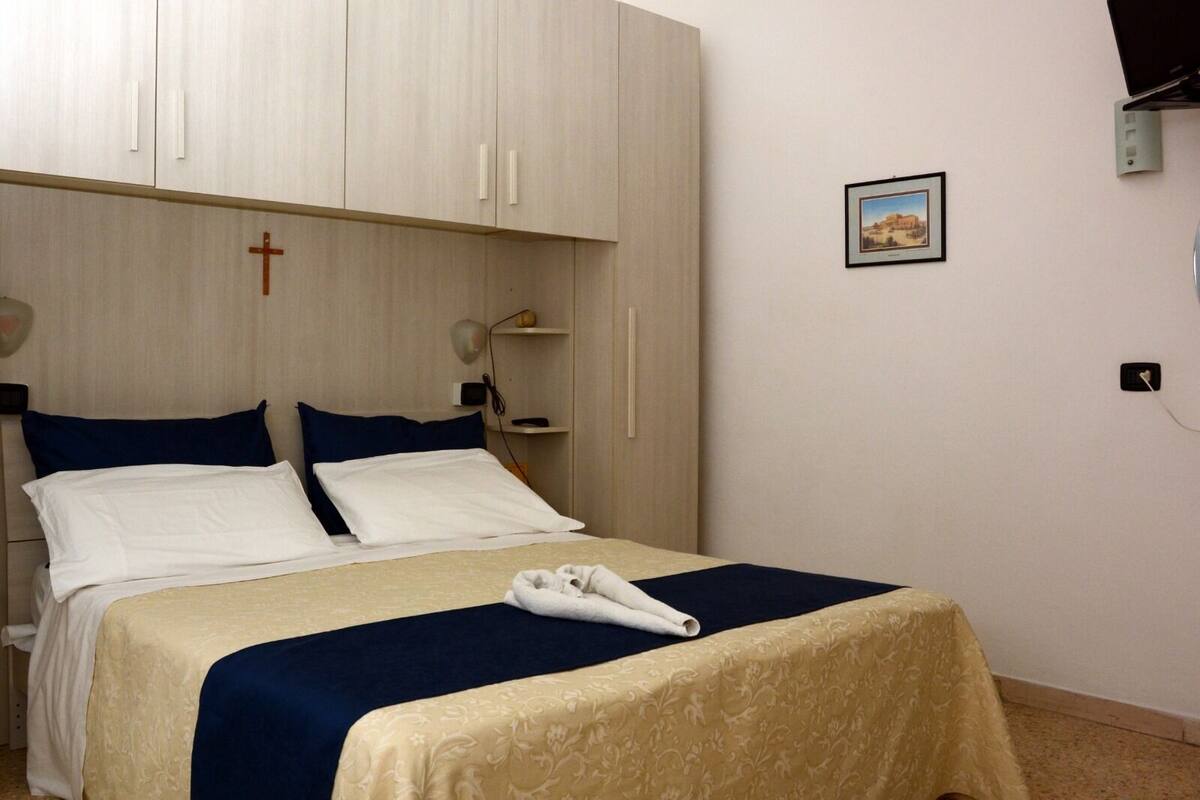 Ein Hotelzimmer mit Bett, Schrank, Nachttisch, Lampe und einem gerahmten Bild an der Wand.