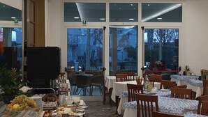 A restaurant with multiple tables and chairs, a buffet with various food items, and large windows with a view of the outside. - Hotel Dea della Salute (Bellaria-Igea Marina)