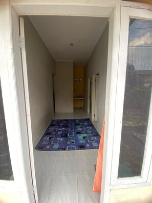 A narrow hallway with a tiled floor, a patterned rug, and a door leading to another room. - Kenangan Guest House (Sabang)