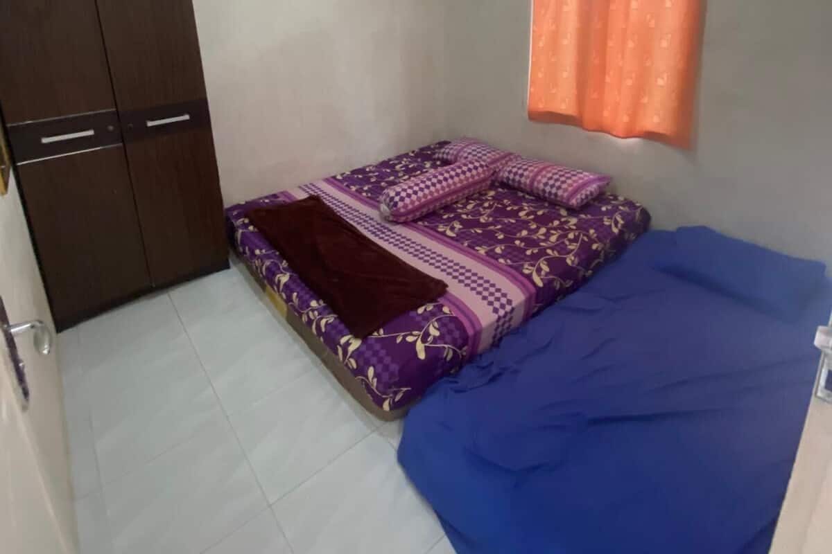 Une petite chambre à coucher, bien éclairée, avec un lit, une armoire et une fenêtre avec des rideaux.