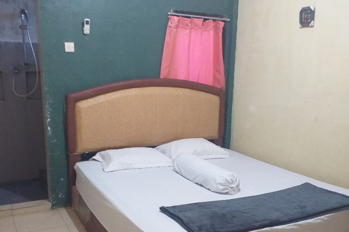 Un lit simple avec une tête de lit en bois, un matelas blanc et une couverture bleue. Un climatiseur mural est fixé au-dessus du lit.