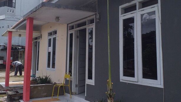 A residential building with a covered porch, a single window, and a small garden area with plants and a chair. - Kenangan Guest House (Sabang)