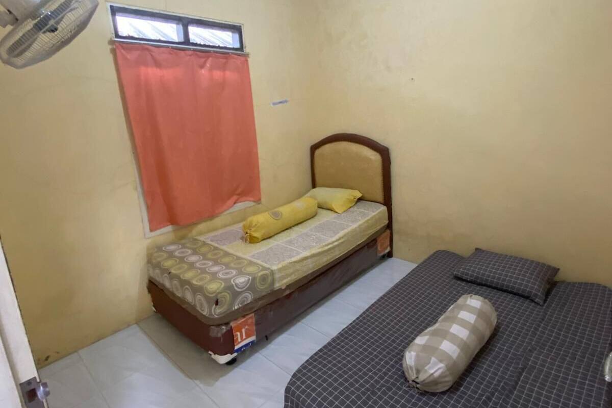 Une petite pièce avec un lit, une fenêtre avec des rideaux, un ventilateur de plafond et un sol carrelé.